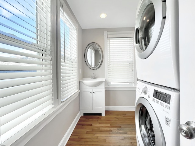 clothes washing area with baseboards, light wood-style flooring, cabinet space, a sink, and stacked washer and dryer