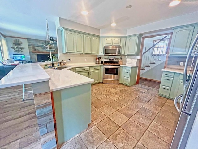 kitchen with green cabinetry, a breakfast bar, a peninsula, a sink, and appliances with stainless steel finishes