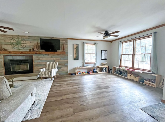 living area featuring a tile fireplace, crown molding, ceiling fan, and wood finished floors