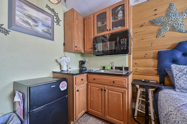 kitchen featuring black appliances, glass insert cabinets, dark countertops, and a sink