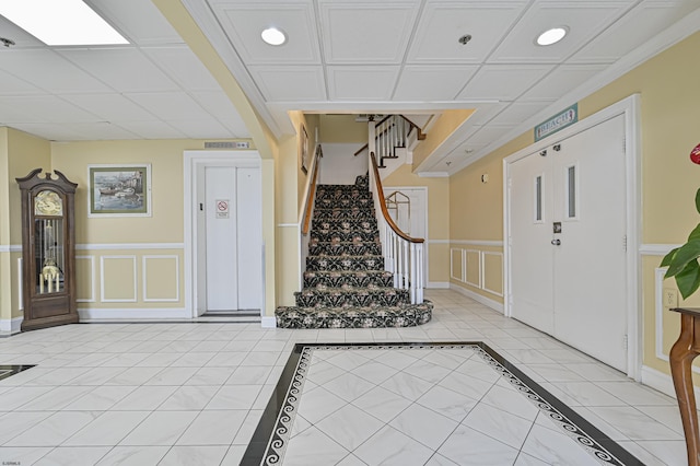 foyer entrance featuring stairway, a wainscoted wall, elevator, light tile patterned flooring, and a decorative wall