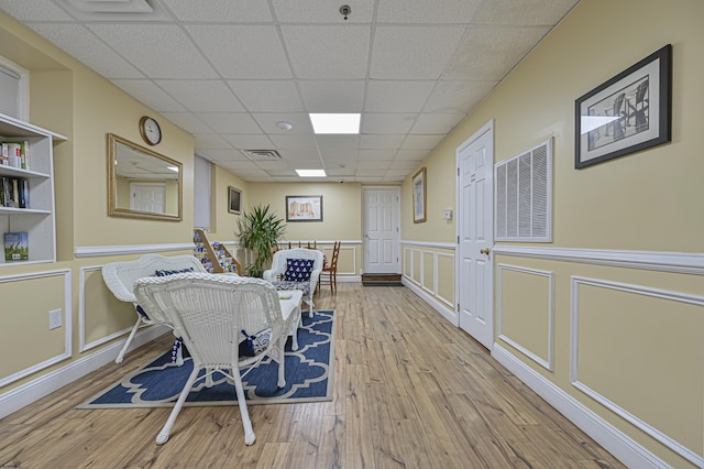 dining space featuring a drop ceiling, visible vents, wood finished floors, and a decorative wall