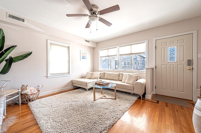 living room with light wood-type flooring, visible vents, baseboards, and a ceiling fan