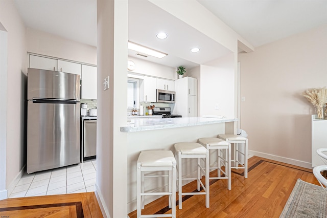 kitchen featuring visible vents, appliances with stainless steel finishes, white cabinetry, a kitchen breakfast bar, and tasteful backsplash