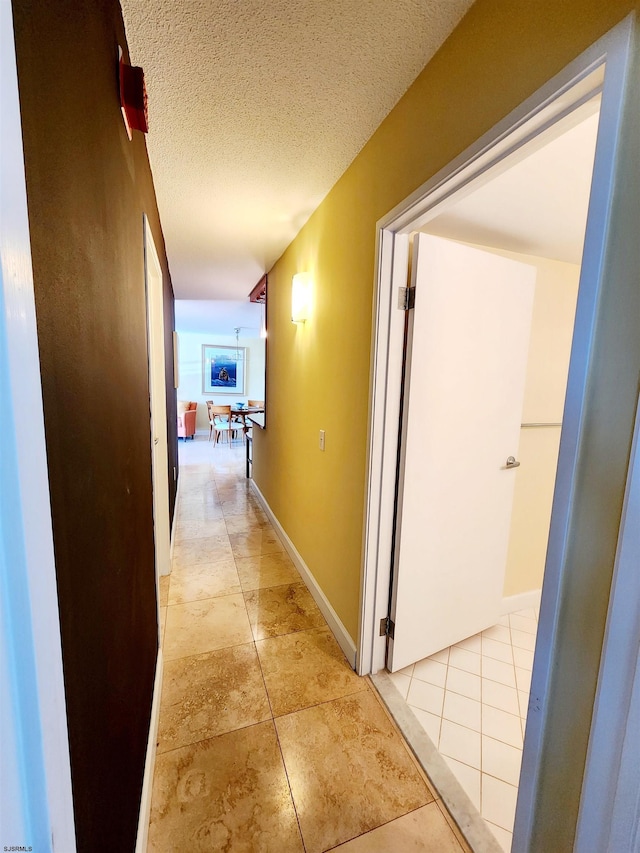 hallway featuring light tile patterned floors, a textured ceiling, and baseboards