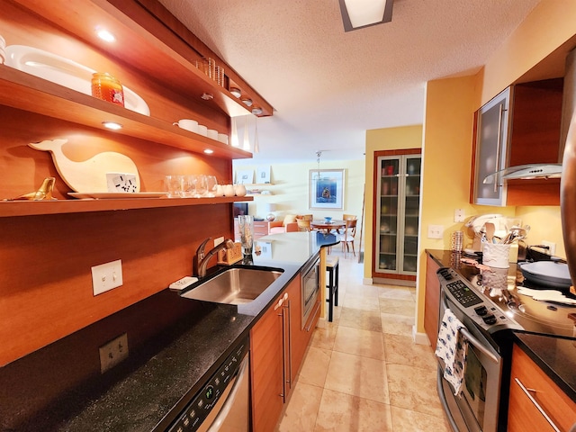 kitchen with a sink, stainless steel appliances, a textured ceiling, and brown cabinetry