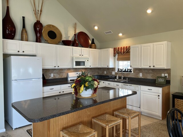 kitchen featuring a breakfast bar area, lofted ceiling, light tile patterned floors, white appliances, and a sink