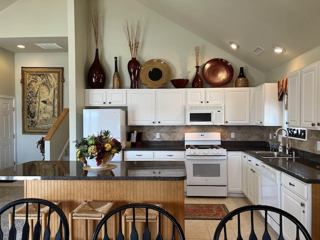 kitchen featuring a breakfast bar, a sink, white appliances, light tile patterned floors, and vaulted ceiling