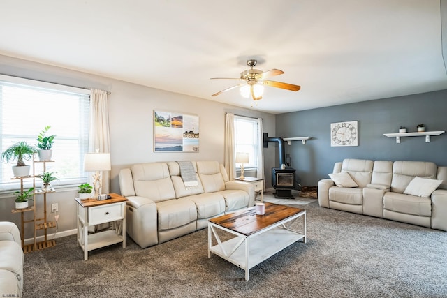 carpeted living area with a wealth of natural light, baseboards, a ceiling fan, and a wood stove