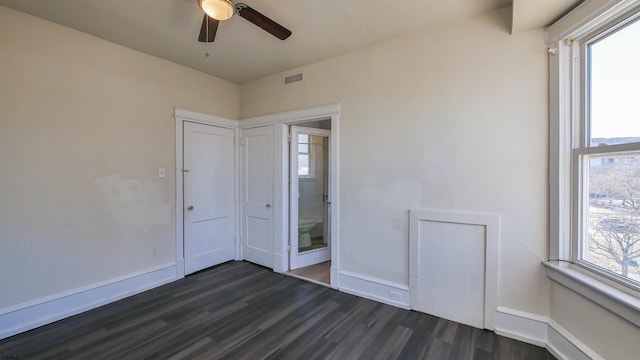 unfurnished bedroom featuring dark wood-style floors, visible vents, multiple windows, and baseboards