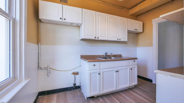 kitchen with a sink, a wainscoted wall, light wood-type flooring, and white cabinetry