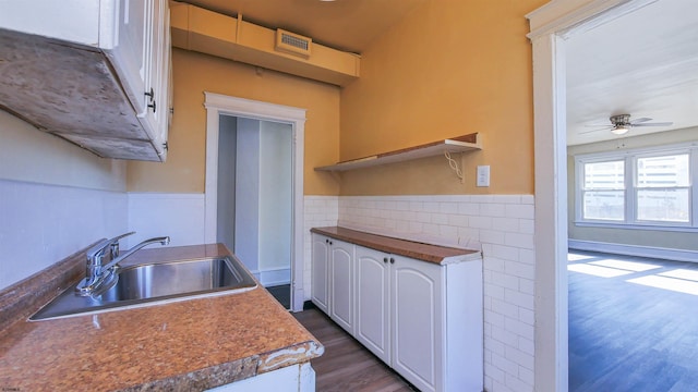 kitchen with a sink, tile walls, white cabinets, wainscoting, and dark wood-style flooring