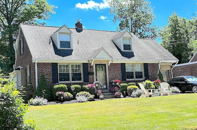 cape cod home featuring a front yard, brick siding, roof with shingles, and a chimney