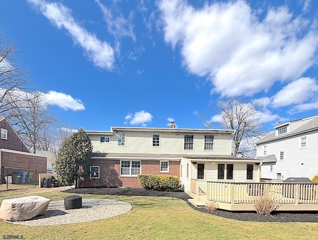 rear view of house with a lawn, a deck, and brick siding