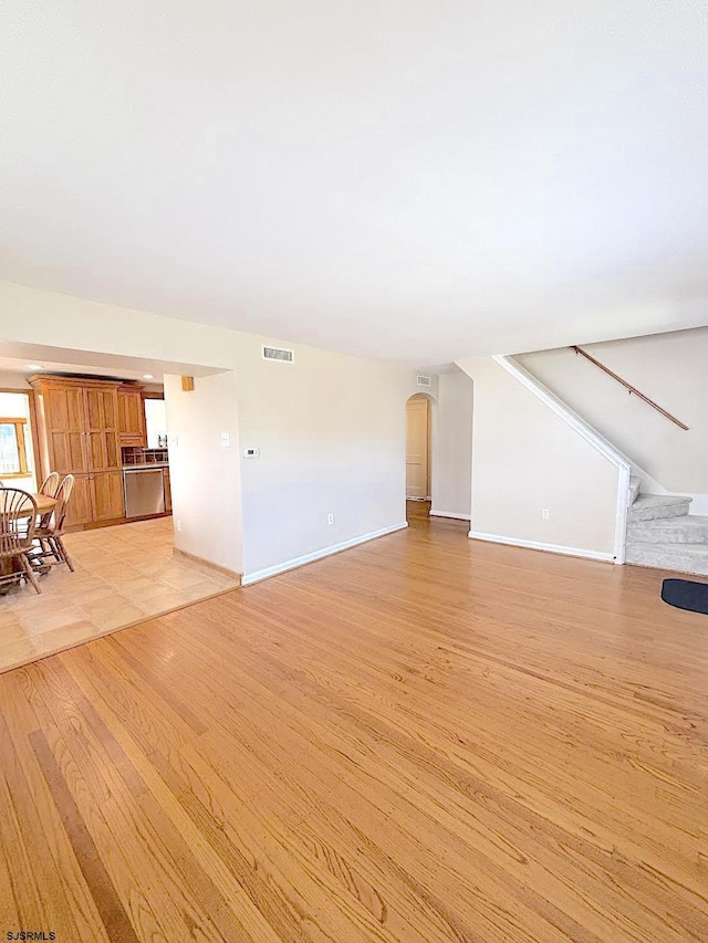 unfurnished living room with visible vents, light wood-type flooring, and baseboards