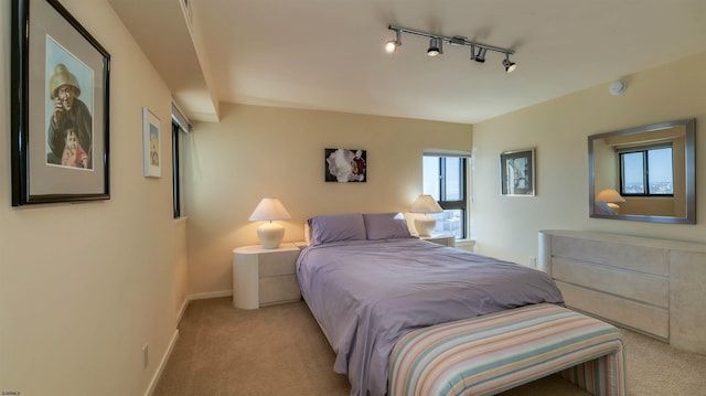 bedroom featuring rail lighting, light colored carpet, and baseboards