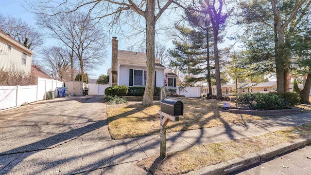 view of front of house with driveway, a chimney, and fence