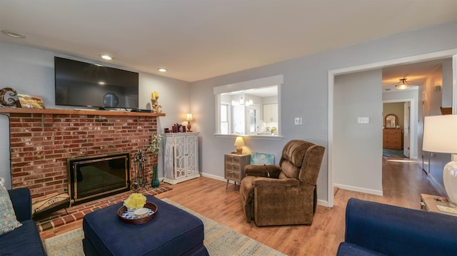 living room featuring a brick fireplace, baseboards, recessed lighting, wood finished floors, and a notable chandelier