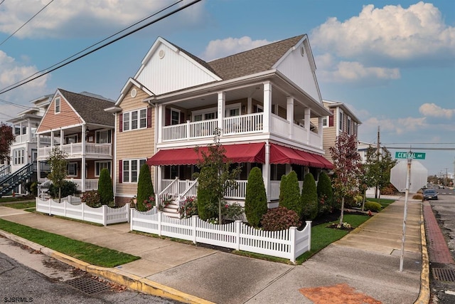 view of front facade with a balcony, a fenced front yard, and a shingled roof