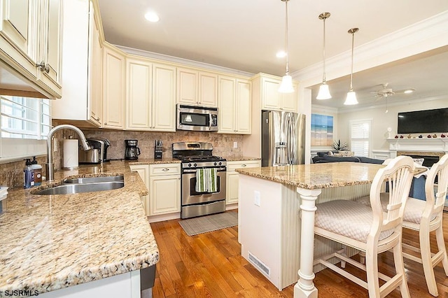 kitchen featuring crown molding, open floor plan, a breakfast bar, stainless steel appliances, and a sink