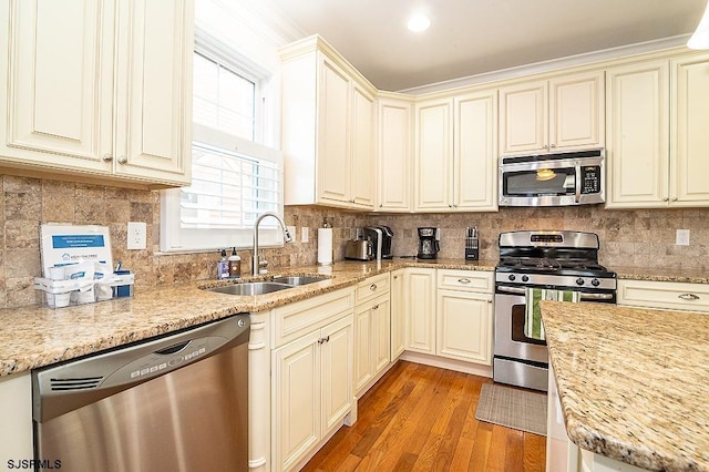 kitchen with light wood finished floors, backsplash, cream cabinetry, stainless steel appliances, and a sink