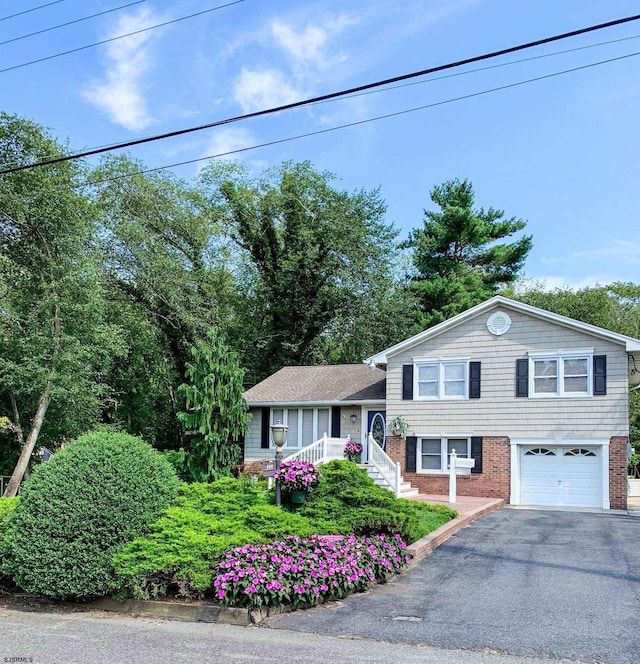 split level home featuring a porch, aphalt driveway, a garage, and brick siding