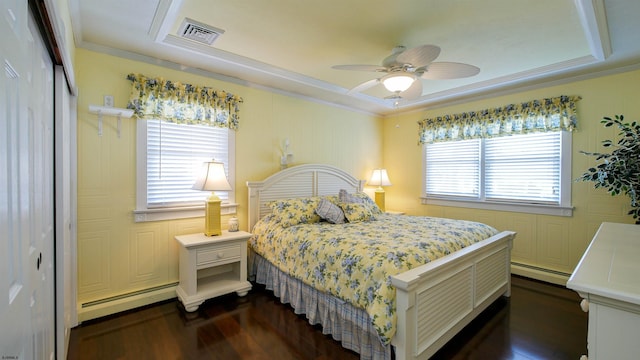 bedroom with dark wood finished floors, visible vents, baseboard heating, and a tray ceiling