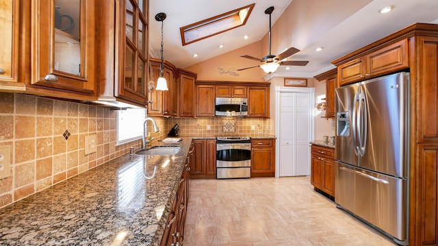 kitchen with brown cabinetry, stainless steel appliances, dark stone counters, and a sink