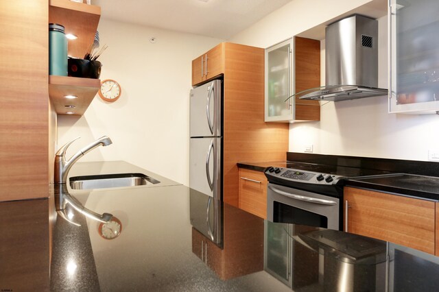 kitchen featuring modern cabinets, a sink, stainless steel appliances, brown cabinetry, and wall chimney range hood