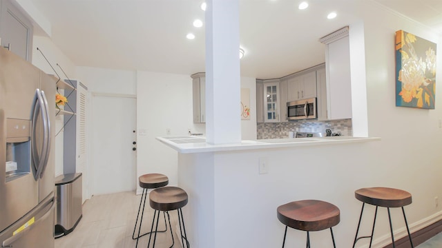 kitchen featuring glass insert cabinets, stainless steel appliances, a kitchen bar, and tasteful backsplash