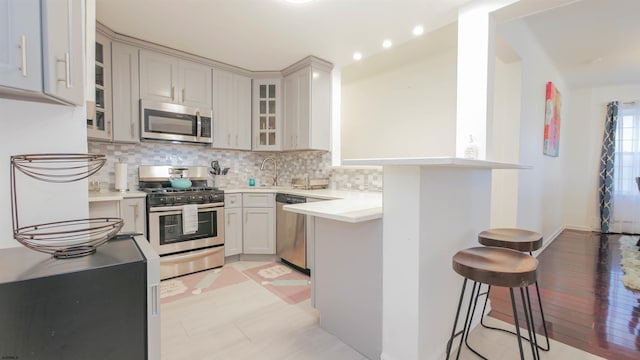 kitchen with a kitchen bar, tasteful backsplash, appliances with stainless steel finishes, light countertops, and glass insert cabinets