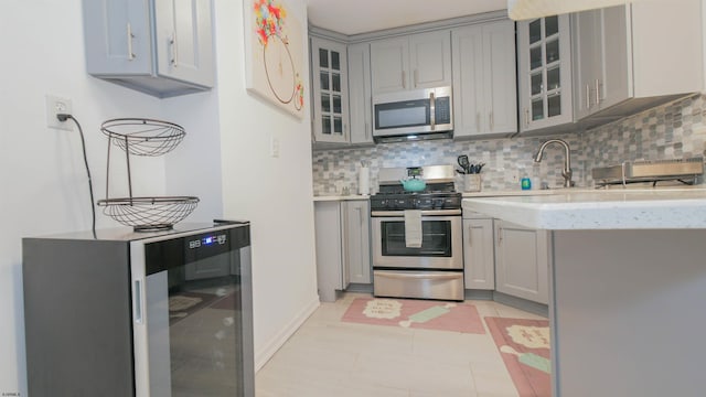 kitchen featuring tasteful backsplash, beverage cooler, gray cabinets, and appliances with stainless steel finishes