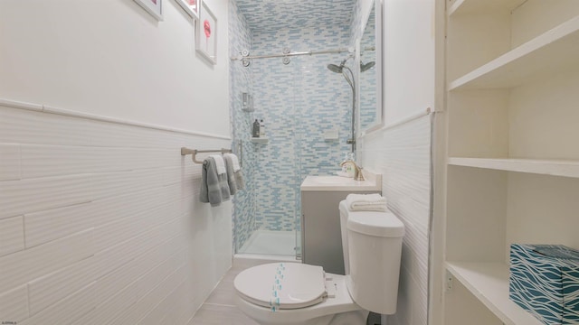 full bathroom featuring a stall shower, a sink, wainscoting, tile walls, and toilet