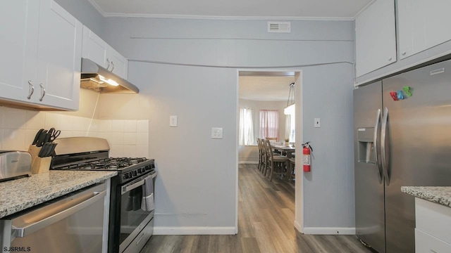 kitchen with under cabinet range hood, backsplash, appliances with stainless steel finishes, crown molding, and dark wood-style flooring