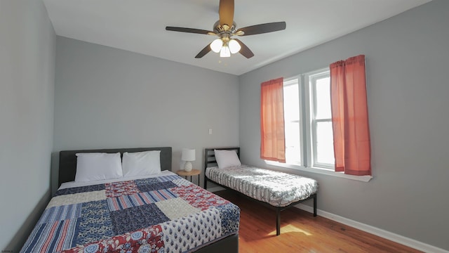 bedroom featuring a ceiling fan, multiple windows, wood finished floors, and baseboards