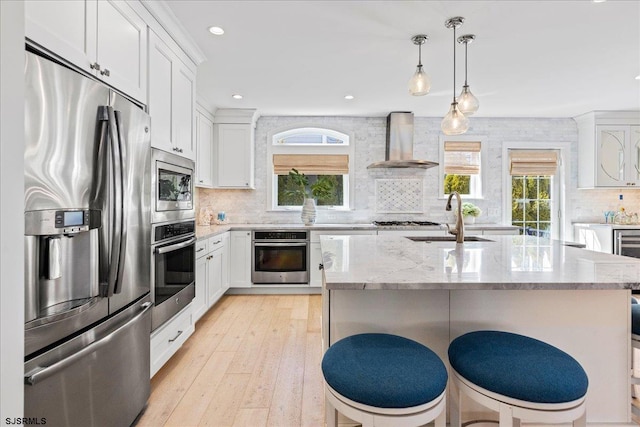 kitchen featuring light stone counters, a sink, decorative backsplash, appliances with stainless steel finishes, and wall chimney range hood