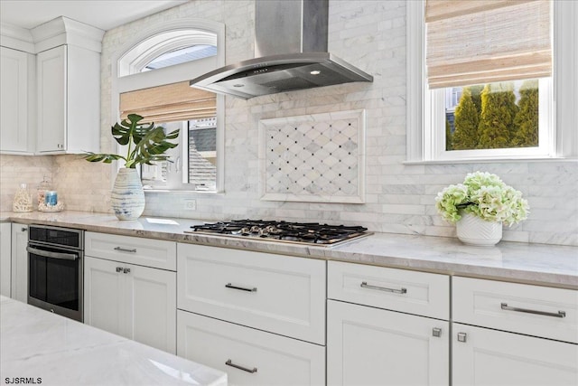 kitchen with a healthy amount of sunlight, white cabinetry, stainless steel appliances, and wall chimney exhaust hood