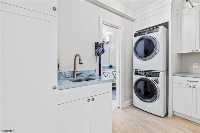 laundry room with cabinet space, light wood-type flooring, stacked washer / drying machine, and a sink