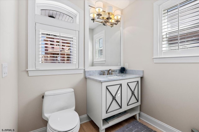 half bathroom with baseboards, toilet, an inviting chandelier, and vanity