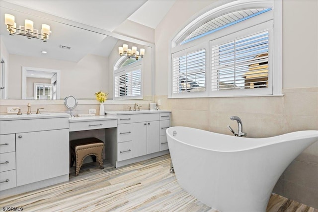 full bathroom with a soaking tub, visible vents, two vanities, and a sink