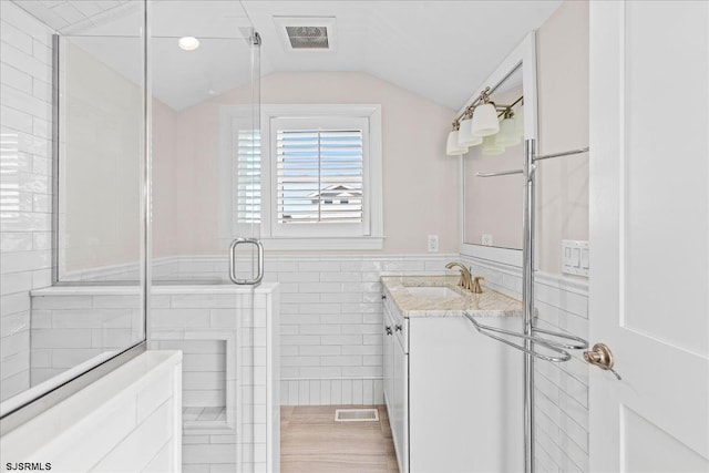 bathroom featuring visible vents, lofted ceiling, tile walls, tiled shower, and vanity