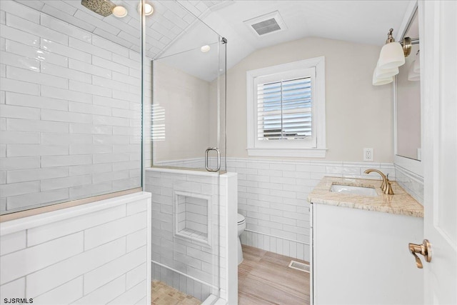 full bathroom with visible vents, toilet, vaulted ceiling, tiled shower, and vanity