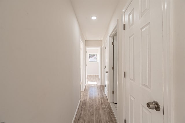 hallway featuring attic access, baseboards, and light wood finished floors