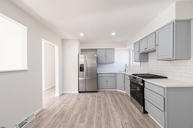 kitchen with visible vents, backsplash, gray cabinetry, stainless steel appliances, and a sink