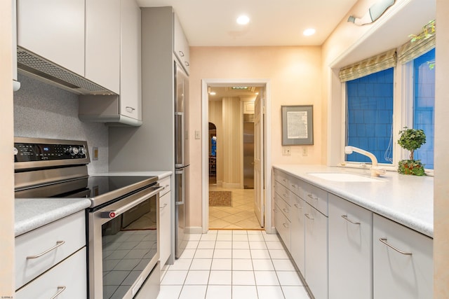 kitchen featuring light countertops, light tile patterned floors, range hood, appliances with stainless steel finishes, and a sink