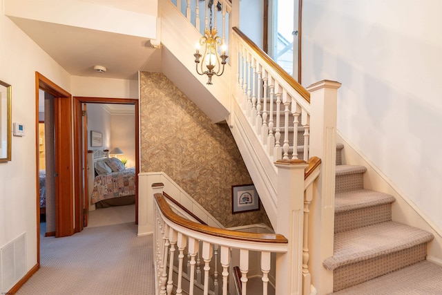 stairs featuring a chandelier, visible vents, wallpapered walls, and carpet