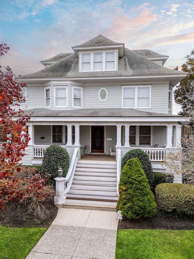 american foursquare style home with a porch and roof with shingles