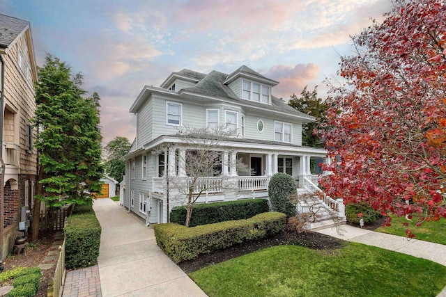 american foursquare style home with a porch, a front lawn, and an outdoor structure