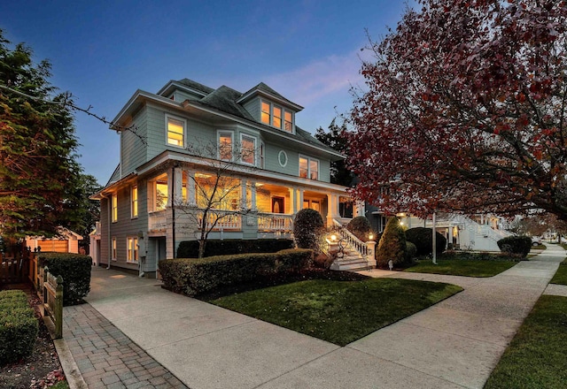 american foursquare style home with a front yard, fence, and covered porch