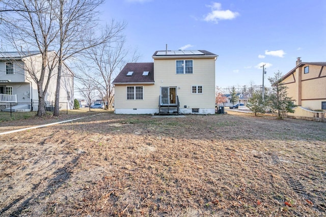 rear view of house with fence, roof mounted solar panels, and crawl space